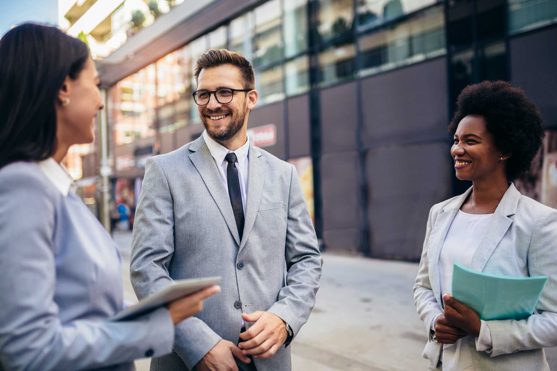 Three young business professionals talk outside of an office building